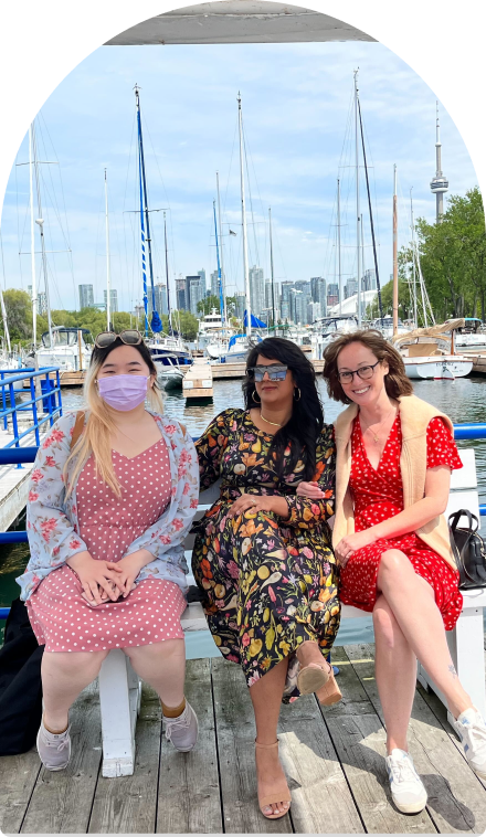 Three employees on a boat dock posing for a photo with the CN Tower in the background.
