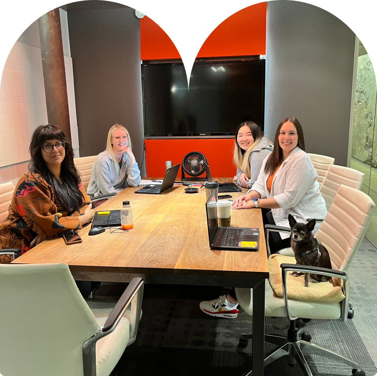 Four employees and a small dog sitting around a table in a meeting room.