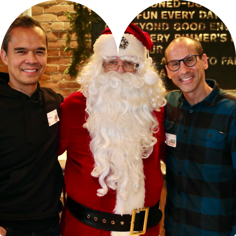 Man dressed as Santa posing for a photo with a person on either side of him.