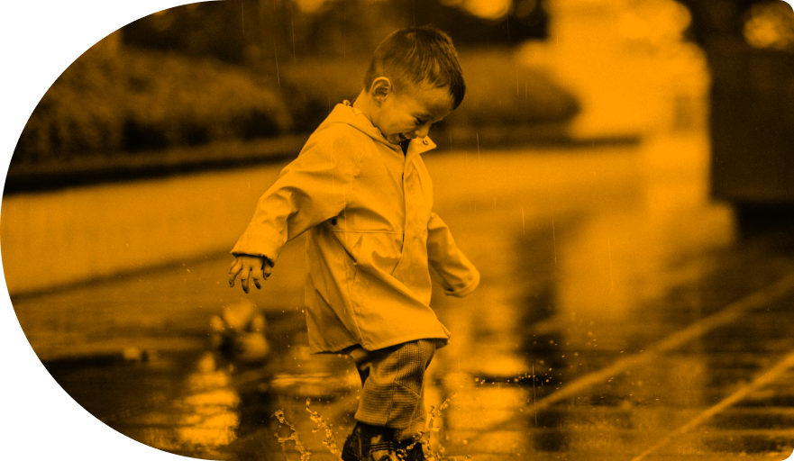 Toddler boy in a rain coat splashing a puddle with his shoes while it rains