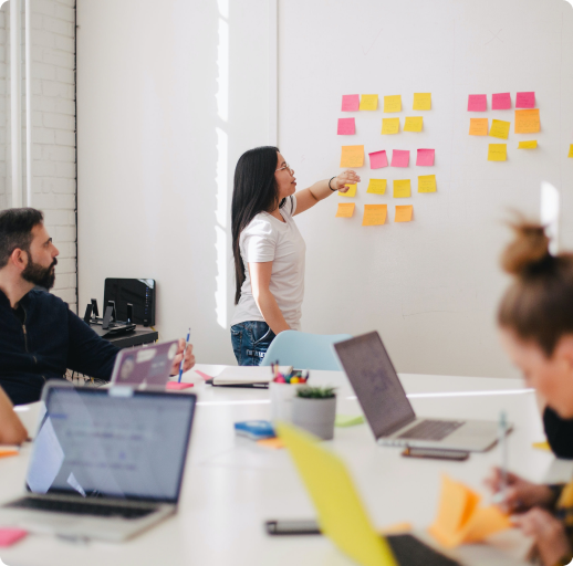 Woman presenting work with sticky notes in front of colleagues in a meeting room.