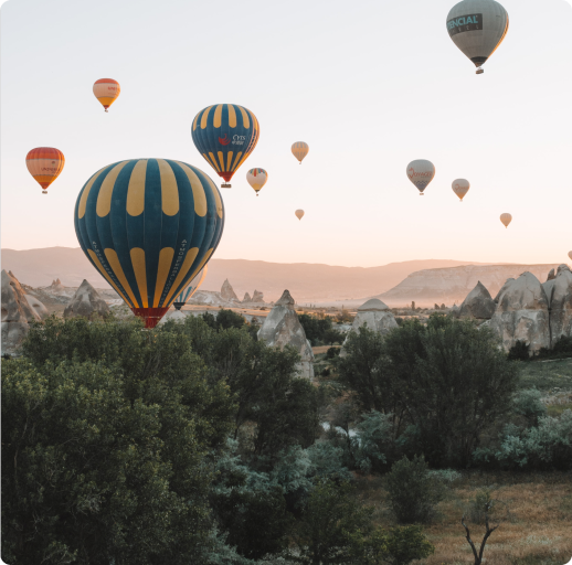 Multicoloured hot air balloons floating in a rocky landscape with trees.