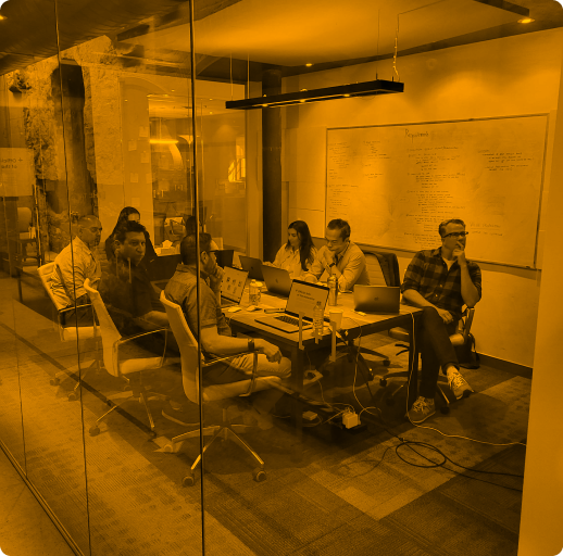 Employees sitting in a meeting room with their laptops open.