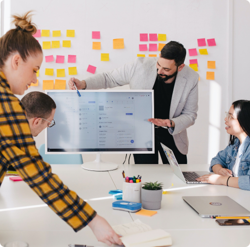 Man presenting work from a monitor screen to colleagues in a meeting room.